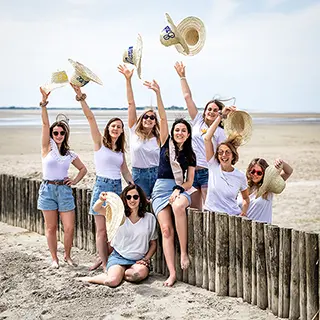 Dans un geste de célébration et d'exubérance, un groupe d'amies lance leurs chapeaux de paille en l'air sur une plage, capturant un moment de pur bonheur et de liberté.