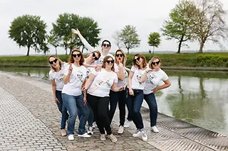 Un groupe de femmes en t-shirts blancs et lunettes de soleil adopte une pose dynamique et confiante sur le chemin pavé le long de la rivière, reflétant un esprit de camaraderie et d'amusement.