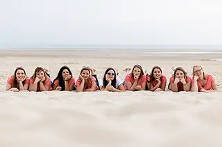Groupe de femmes allongées sur le sable, souriant à la caméra