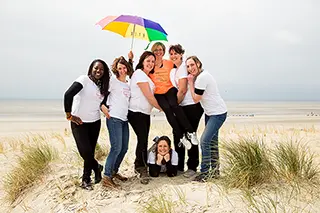 Groupe de femmes éclatantes de joie sous un parapluie multicolore sur une plage