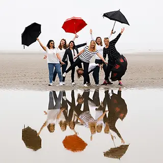 Groupe de femmes avec des parapluies colorés se reflétant sur la plage humide