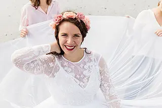 Mariée souriante entourée d'un voile blanc sur la plage