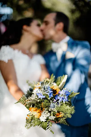Mariés s’embrassant tendrement derrière un bouquet de mariage flou