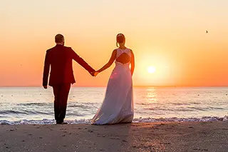 Silhouette des mariés se tenant par la main devant le coucher de soleil sur la plage