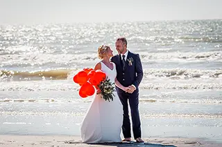 Mariés en balade romantique sur la plage avec des ballons rouges