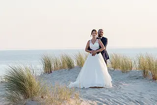 Mariés enlacés sur une dune de plage au coucher du soleil
