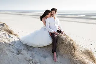 Couple de mariés se détendant sur une dune avec la plage de Fort-Mahon-Plage en arrière-plan.