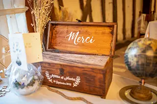 Coffre en bois avec l'inscription 'Merci' utilisé pour la collecte des cadeaux des invités lors d'une réception de mariage, entouré de décorations et d'un globe.