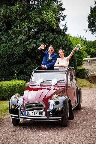 Mariés joyeux saluant depuis une voiture de collection décorée