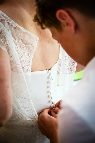 Gros plan sur les mains fermant la robe de la mariée