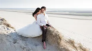 Couple marié assis sur une dune avec une plage en arrière-plan