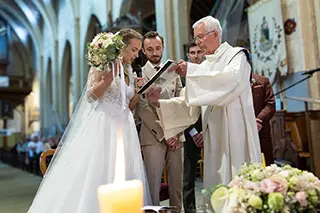La mariée et le marié durant la cérémonie de mariage à l'église, en présence du prêtre et d'un microphone, dans un moment solennel.
