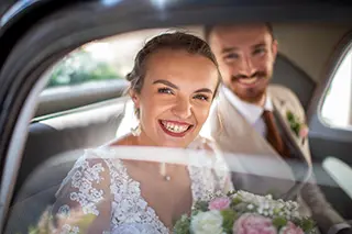 Mariée rayonnante et marié souriant, pris en photo à travers la vitre d'une voiture.
