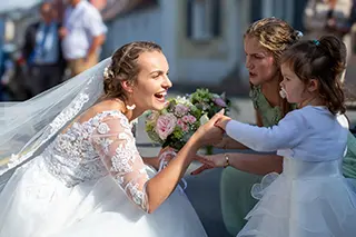 Mariée souriante tenant la main d'une jeune fille en robe blanche pendant un moment de convivialité à l'extérieur.