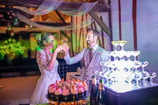 Les mariés trinquent avec des coupes de champagne devant la pièce montée et les pâtisseries lors de la réception de mariage.