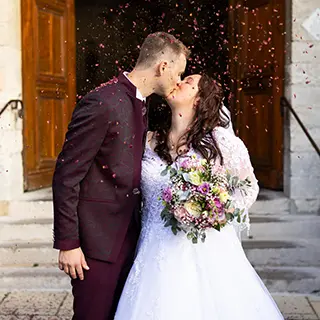 Mariés s'embrassant à la sortie de l'église sous une pluie de pétales de roses.