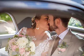 Couple de marié s'embrassant à l'arrière d'une voiture de collection.