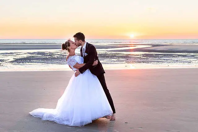 Jeunes mariés s'embrassant sur une plage au coucher du soleil