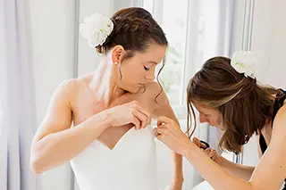 Une aide habillant la mariée avec soin