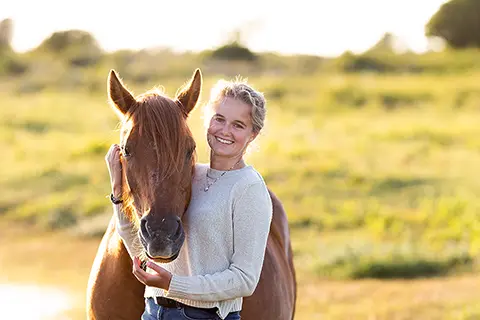 Femme souriante tenant son cheval par la bride au coucher du soleil
