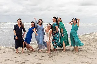 Groupe de femmes joyeuses en robes colorées sur une plage venteuse.