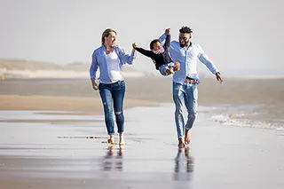 Deux adultes et un enfant courant main dans la main sur une plage