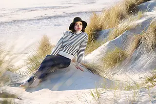Femme en pull rayé et jean's assise sur une dune de sable