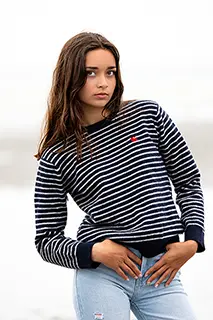 Jeune femme en pull à rayures et jeans posant sur un fond flou