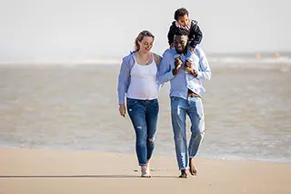 Famille marchant sur la plage, un enfant porté sur les épaules de l'homme