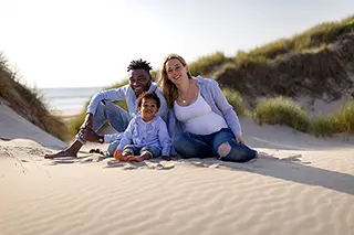 Famille souriante assise sur le sable d'une dune de plage