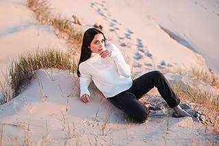 Femme pensive assise sur une dune de sable au coucher du soleil.