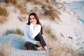 Jeune femme souriante assise sur une dune de sable avec la plage en arrière-plan
