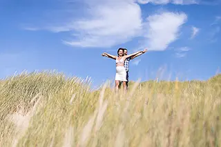 Femme enceinte les bras écartés sur une dune avec ciel bleu en arrière-plan