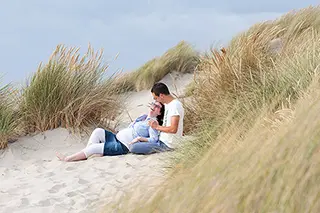 Couple assis sur une dune, homme parlant à sa femme enceinte