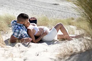 Couple attendrissant allongé sur le sable, homme embrassant le front de la femme enceinte
