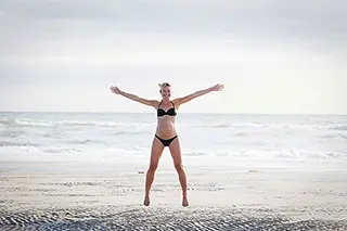 Femme enceinte sautant de joie sur une plage.