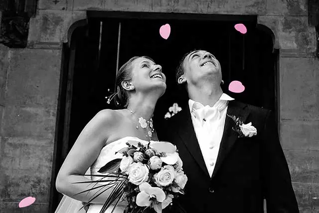 Jeunes mariés souriant sortent de l'église sous une pluie de coeur en papier