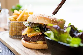 Cheeseburger juteux avec des frites et de la salade servis sur une planche en bois