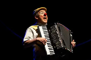 Un clown avec un nez rouge souriant joue de l'accordéon sur la piste de cirque