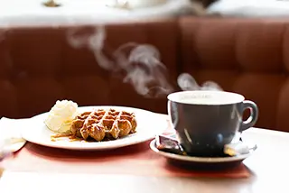 Tasse de café fumante à côté d'une gaufre avec de la crème fouettée sur une table de café
