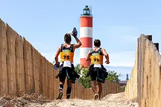 Marathoniens courant près d'un phare sur une piste sableuse