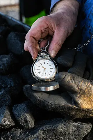 Main gantée tenant un montre à gousset ouverte au milieu de charbons