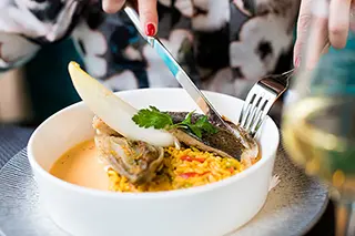 Main tenant un couteau et une fourchette coupant un poisson dans un plat avec riz et une sauce crème
