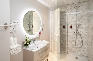 Salle de bain moderne d'hôtel avec miroir rond, douche en verre et serviettes blanches
