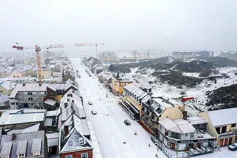 Vue aérienne d'une ville enneigée avec des toits blancs, des rues couvertes de neige et des dunes en arrière-plan sous un ciel brumeux