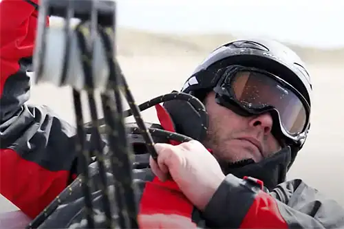 Un homme en veste rouge portant casque et lunette dans un char à voile