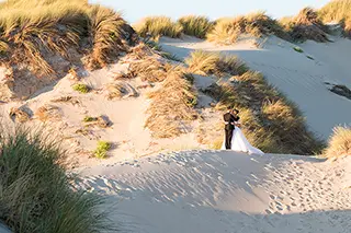 Mariés s'embrassant sur une dune de sable avec vue sur la plage