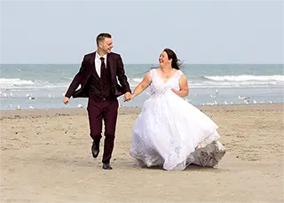 Un jeune couple de mariés courant joyeusement sur une plage de sable de fin