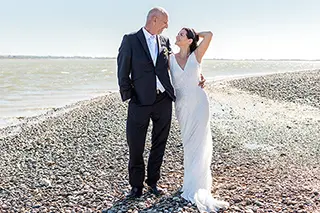Mariés debout sur une plage de galets regardant l'horizon