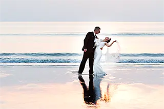 Mariés se tenant debout sur la plage avec leur reflet sur l'eau